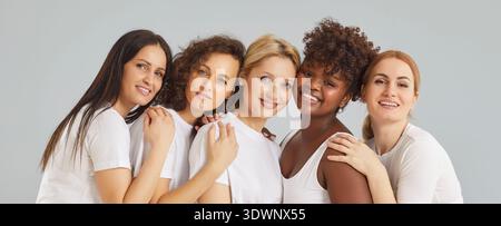 Happy women in white clothes hugging and looking at camera isolated on studio grey background. Stock Photo