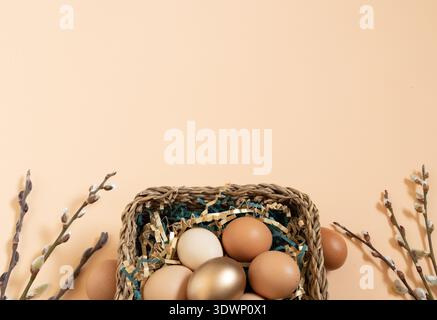 Easter eggs natural and gold in basket with paper filler . Branch of willow catkinsan. Peach fuzz background with copy space. Stock Photo