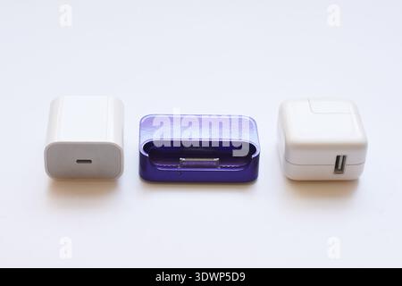 Various iPhone and iPad chargers, cables, and power adapters arranged on a clean white table. Concept of mobile technology, charging accessories Stock Photo