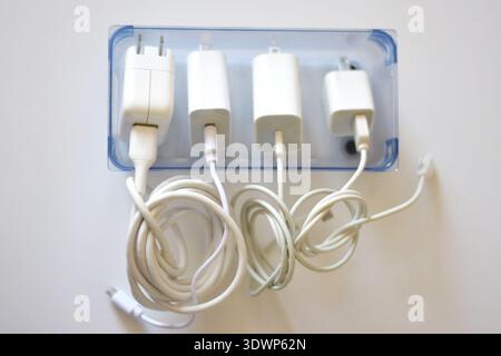 Various iPhone and iPad chargers, cables, and power adapters arranged on a clean white table. Concept of mobile technology, charging accessories Stock Photo