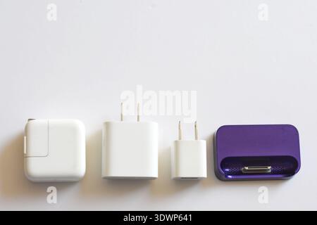 Various iPhone and iPad chargers, cables, and power adapters arranged on a clean white table. Concept of mobile technology, charging accessories Stock Photo