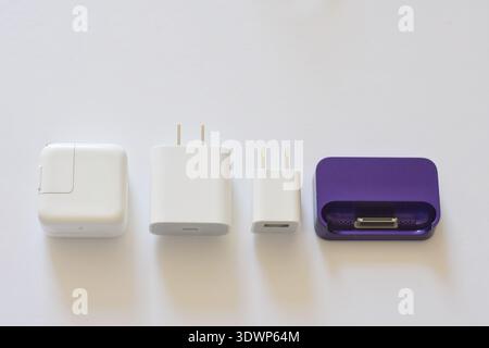 Various iPhone and iPad chargers, cables, and power adapters arranged on a clean white table. Concept of mobile technology, charging accessories Stock Photo