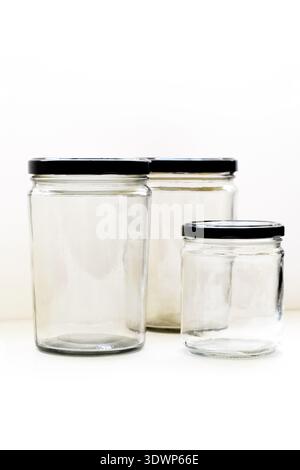 Large and small empty transparent glass bottles with black caps placed on a white table with a clean white background, ideal for cosmetic Stock Photo