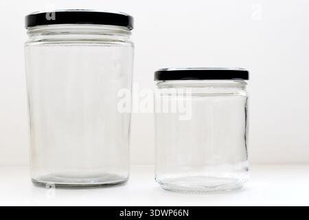 Large and small empty transparent glass bottles with black caps placed on a white table with a clean white background, ideal for cosmetic Stock Photo