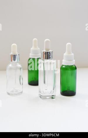 Empty green and transparent glass dropper bottles on a white table with white background, ideal for cosmetic, skincare, essential oil or pharmaceutica Stock Photo