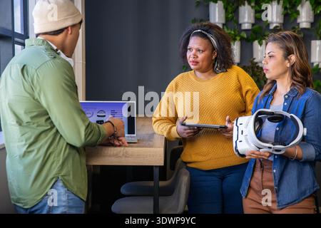 Diverse coworkers leaning around wooden counter in modern office with laptop, tablet, VR headset Stock Photo