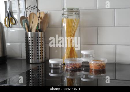 Spaghetti jar and kitchen utensils on modern countertop with spice jars and tile backsplash Stock Photo