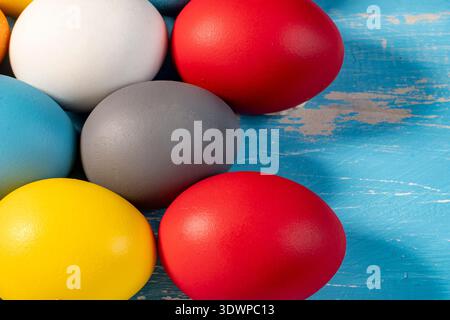 Close-up of brightly colored Easter eggs arranged on a rustic blue wooden surface, highlighting texture, vibrant tones and seasonal holiday concept. Stock Photo