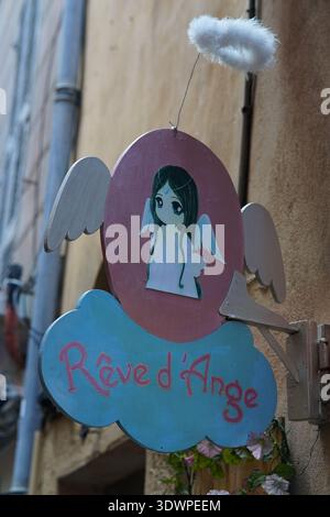 Whimsical hanging sign "Rêve d'Ange" featuring a sweet winged angel girl on a cloud, adorning a charming alley wall in Vieux Nice, France. Stock Photo