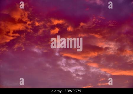 A breathtaking and vibrant natural background featuring a dramatic sunset or sunrise sky. Swirling clouds are painted with intense hues of fiery orang Stock Photo