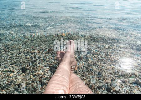 POV view of woman legs submerged in crystal clear Mediterranean water with light refraction. Horizontal summer lifestyle shot Stock Photo
