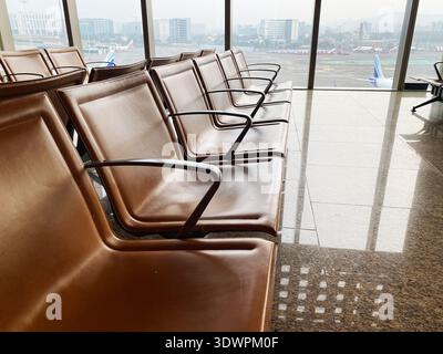 Mumbai, India - October 21, 2025: Leather chairs arranged in a row inside Mumbai International Airport terminal with a view of the runway and parked a Stock Photo