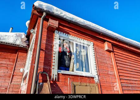 After installing outdoor dome surveillance camera on facade of farmhouse rural resident connects power supply to it Stock Photo