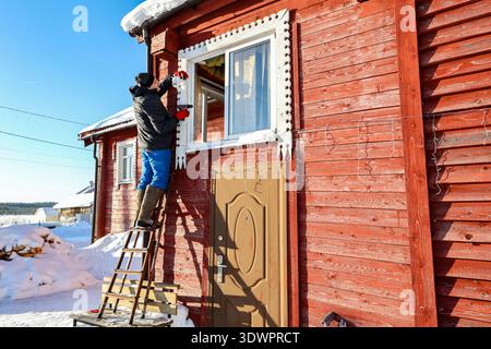 Standing on stepladder homeowner installs dome surveillance camera on outer wall of farm house in winter. Stock Photo