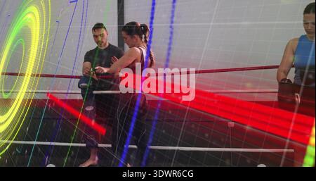 Wrapping coach adjusting center woman in black tank, hand wraps in boxing ring, light overlays Stock Photo