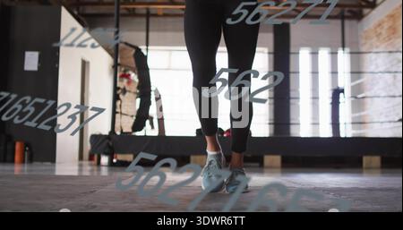 Jumping female in black leggings and shoes skipping on gym mats with numeric decals, ring ropes Stock Photo