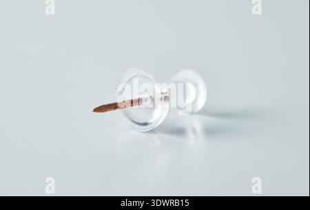 A single transparent map tack with a metal needle point, isolated on a light surface Stock Photo