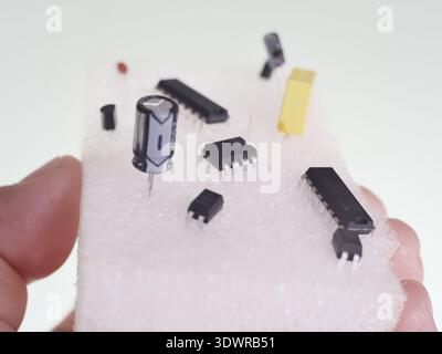 An image of various electronic components embedded on a white sheet of foam, held by a hand. Stock Photo