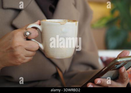 Holding a coffee cup while looking at a smartphone Stock Photo