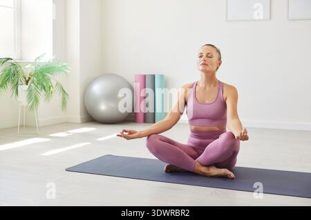 Sporty yogi relaxed woman sitting cross-legged on yoga mat in lotus pose, meditating Stock Photo