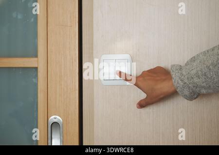 Hand pressing light switch on a wooden door Stock Photo