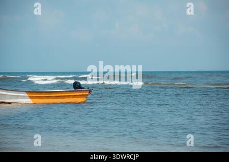 Small orange and white motorboat gently floating in the clear blue ocean with small waves under a bright sky, symbolizing summer relaxation and coasta Stock Photo