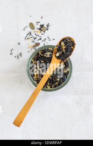 Loose leaf tea in wooden spoon on a glass jar, placed on a white linen cloth with tea leaves scattered around Stock Photo