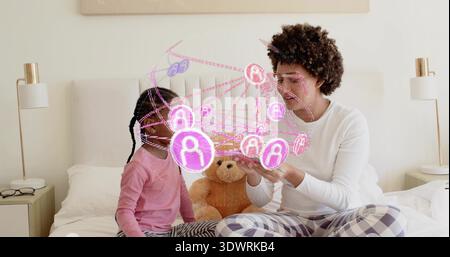Interacting adult woman and daughter touching pink holographic network on bed in bedroom in pajamas Stock Photo