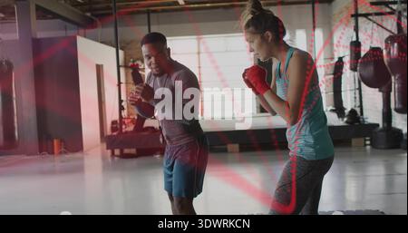 Practicing coach and trainee boxing in loft gym heavy bags, man long-sleeve top, woman red wraps Stock Photo