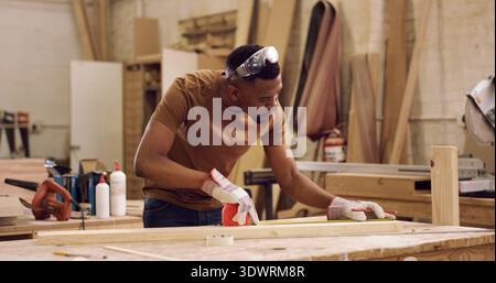 Carpentry, planning and black man with tape measure in workshop, construction process and precision. Tools, woodworking and carpenter with plank for Stock Photo