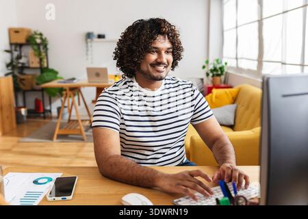 Young Indian man working on desktop computer at home office Stock Photo