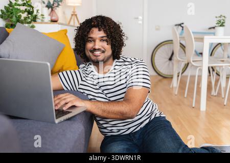 Young Indian man using laptop on sofa at home Stock Photo