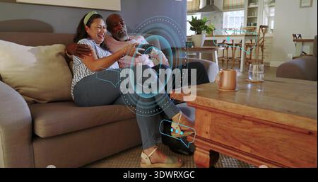 Sitting couple wearing striped blouse and dark polo, holding controller on home sofa with AR UI Stock Photo