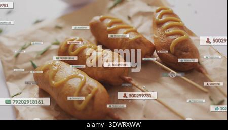 Showing four corn dogs on wooden skewers at kitchen table, with mustard, parchment, herbs, UI tags Stock Photo