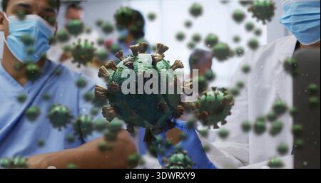 Holding nitrile-gloved hand displaying large green virus model in ward, masked staff in blue scrubs Stock Photo
