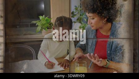 Helping mom in red denim shirt guiding girl writing notebook at dining table, with pink pencil Stock Photo