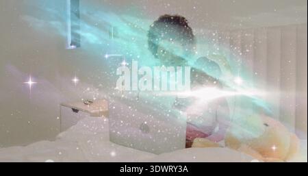 Watching woman and girl in pajamas using laptop in bedroom, with stuffed bear and aurora overlay Stock Photo