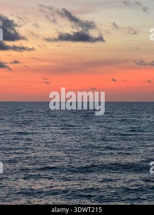 Calm sea at sunset with soft pink and orange sky above the horizon, peaceful seascape with gentle waves and scattered clouds. Stock Photo