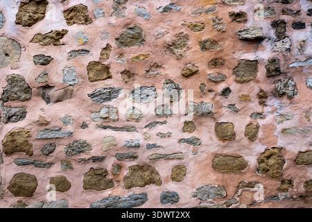 Texture of an ancient stone wall with irregular rocks embedded in weathered pink lime mortar featuring a rustic and traditional masonry style from a Stock Photo