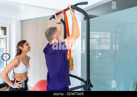 Physiotherapist assisting man doing assisted pull ups for rehabilitation Stock Photo