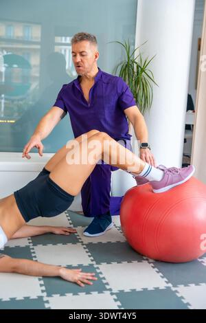 Physiotherapist guiding patient performing rehabilitation exercise with stability ball Stock Photo