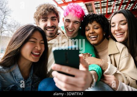 Diverse group of students sitting on campus stairs using phones together Stock Photo