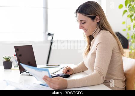 Young adult caucasian businesswoman using calculator at home office Stock Photo