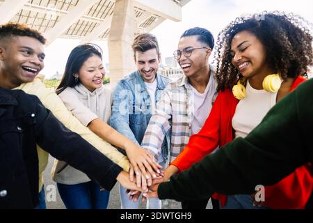 Group of cheerful gen z students stacking hands standing together outdoor Stock Photo