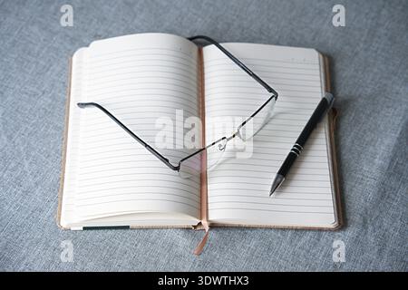 On the table are an open lined notebook, a black pen, and thin-framed glasses. High quality photo Stock Photo