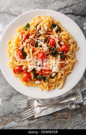 Italian tagliatelle pasta served on a white plate with roasted cherry tomatoes, white beans, spinach and grated parmesan closeup on the plate on the t Stock Photo
