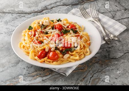 Italian tagliatelle pasta with white beans, cherry tomatoes, parmesan and spinach close-up in a plate on the table. Horizontal Stock Photo
