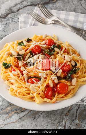 Italian tagliatelle pasta served on a white plate with roasted cherry tomatoes, white beans, spinach and grated parmesan closeup on the plate on the t Stock Photo