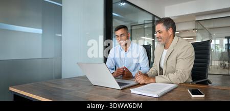 Two busy happy business men working together talking using laptop in office. Stock Photo