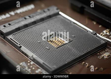 empty black plastic cpu socket on motherboard surface, small contact holes and central electronic components, top view closeup with soft focus Stock Photo